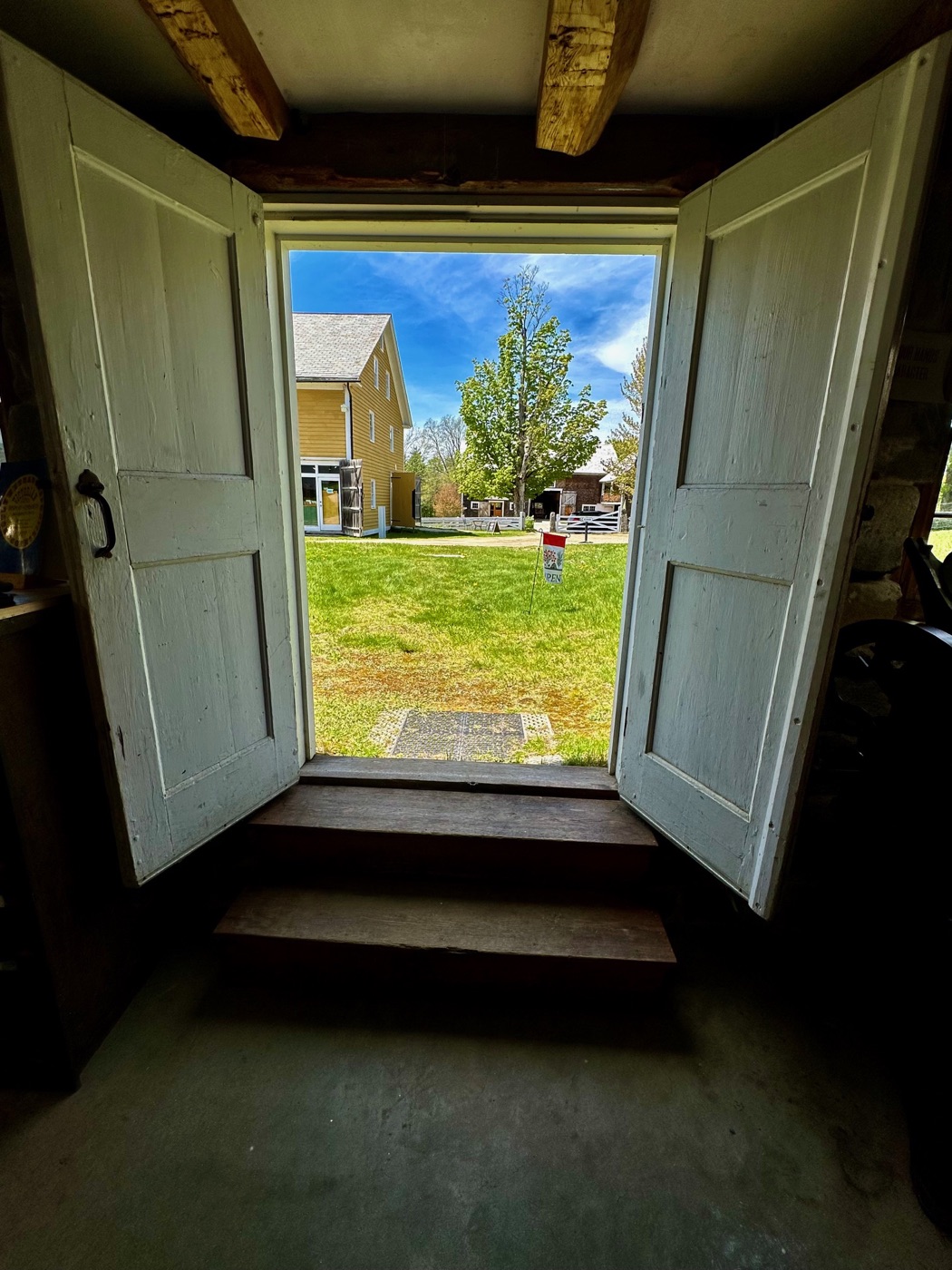 Double doors open from a dark interior onto the green lawn at Canterbury Shaker Village.