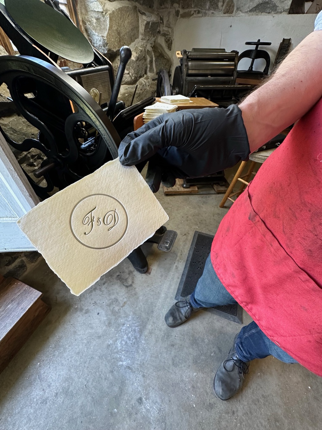 A gloved hand lifts a sheet of handmade paper embossed with a monogram at a Canterbury Shaker Village papermaking demonstration.