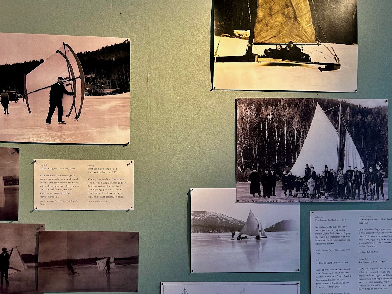 A museum wall of sepia and black and white photographs showing skate sailing and ice boating on frozen Maine lakes and ponds, with typed exhibit labels between them.