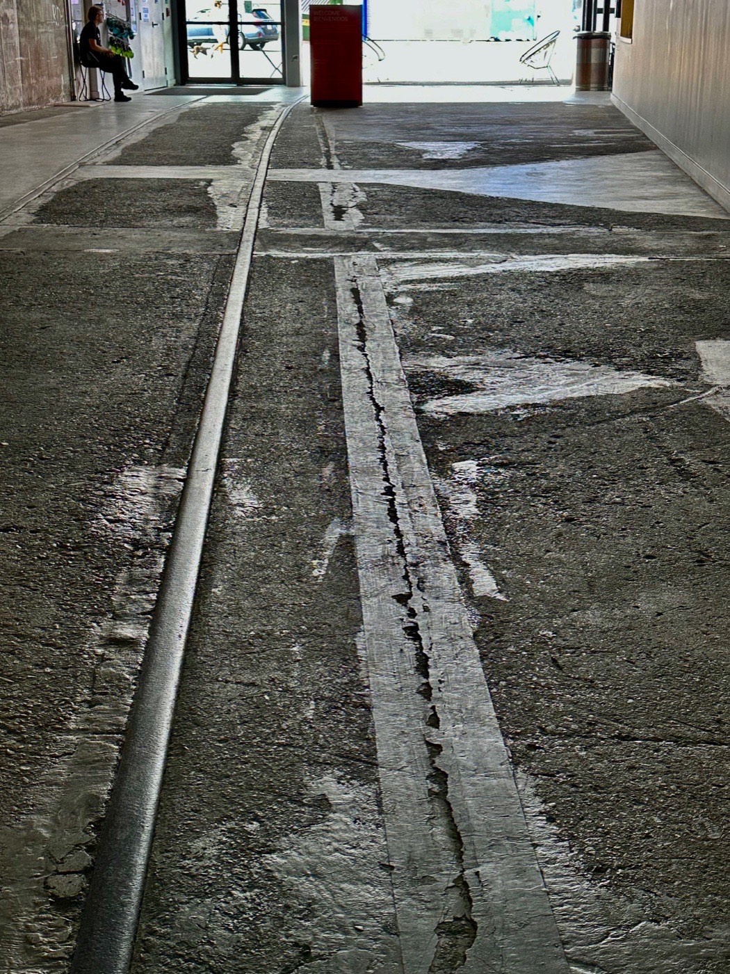 Old rail tracks embedded in the concrete floor of the ICA Watershed, a former copper pipe factory, leading toward the entrance.