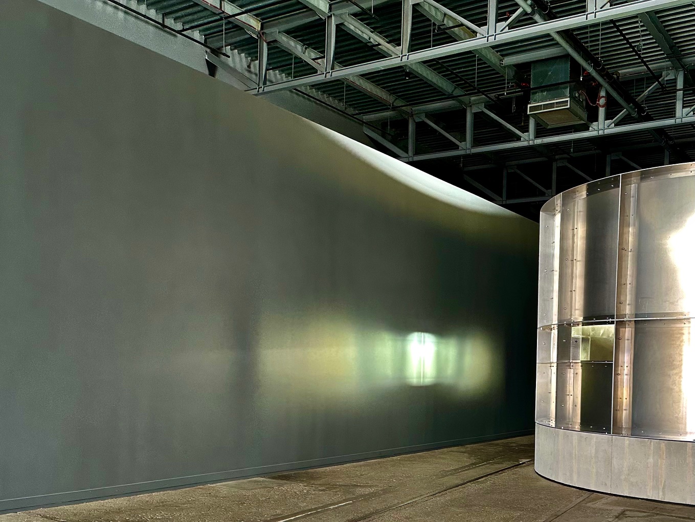 Light from Lucy Raven's kinetic sculpture Hardpan sweeping across a curved gray wall at the ICA Watershed.