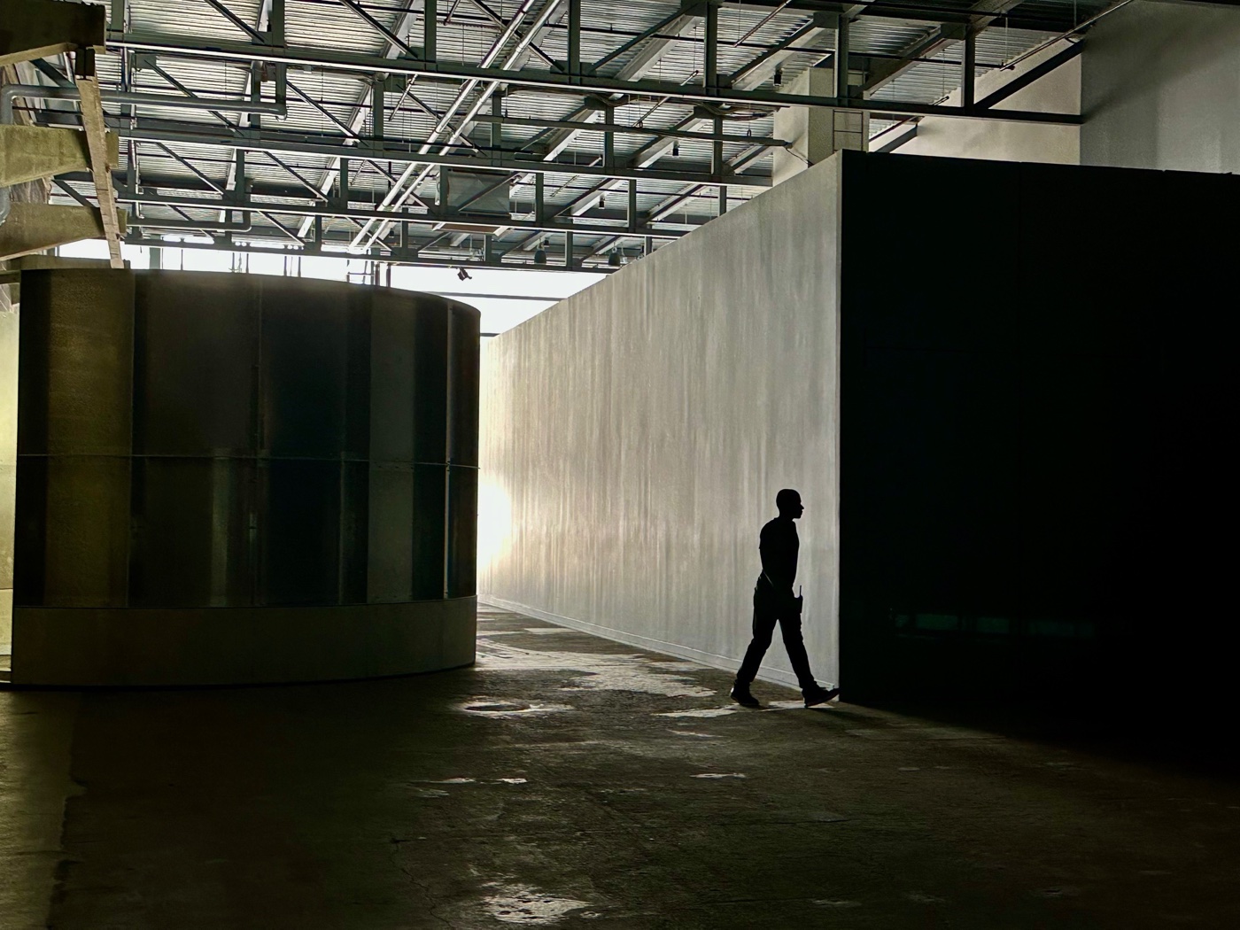 A silhouetted figure walking between Hardpan's aluminum cylinder and a glowing wall at the ICA Watershed.