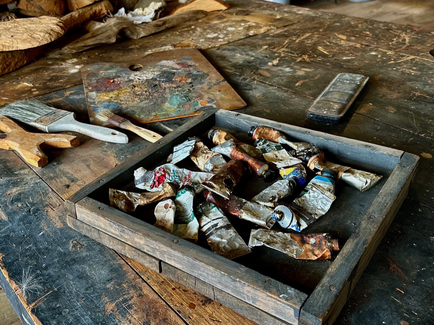 A wooden tray of crushed and dried oil paint tubes beside a spattered palette and two brushes on the worn workbench in Bernard Langlais&rsquo;s studio.