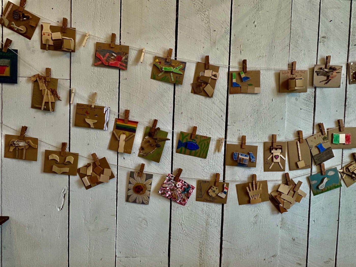 Small visitor made collages of wood scraps and paint, pinned with clothespins to lines strung across a white board wall at the Langlais Art Preserve.