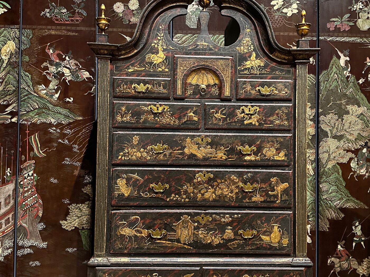 An ornate black-and-gold japanned high chest against floral wallpaper at the Museum of Fine Arts, Boston.