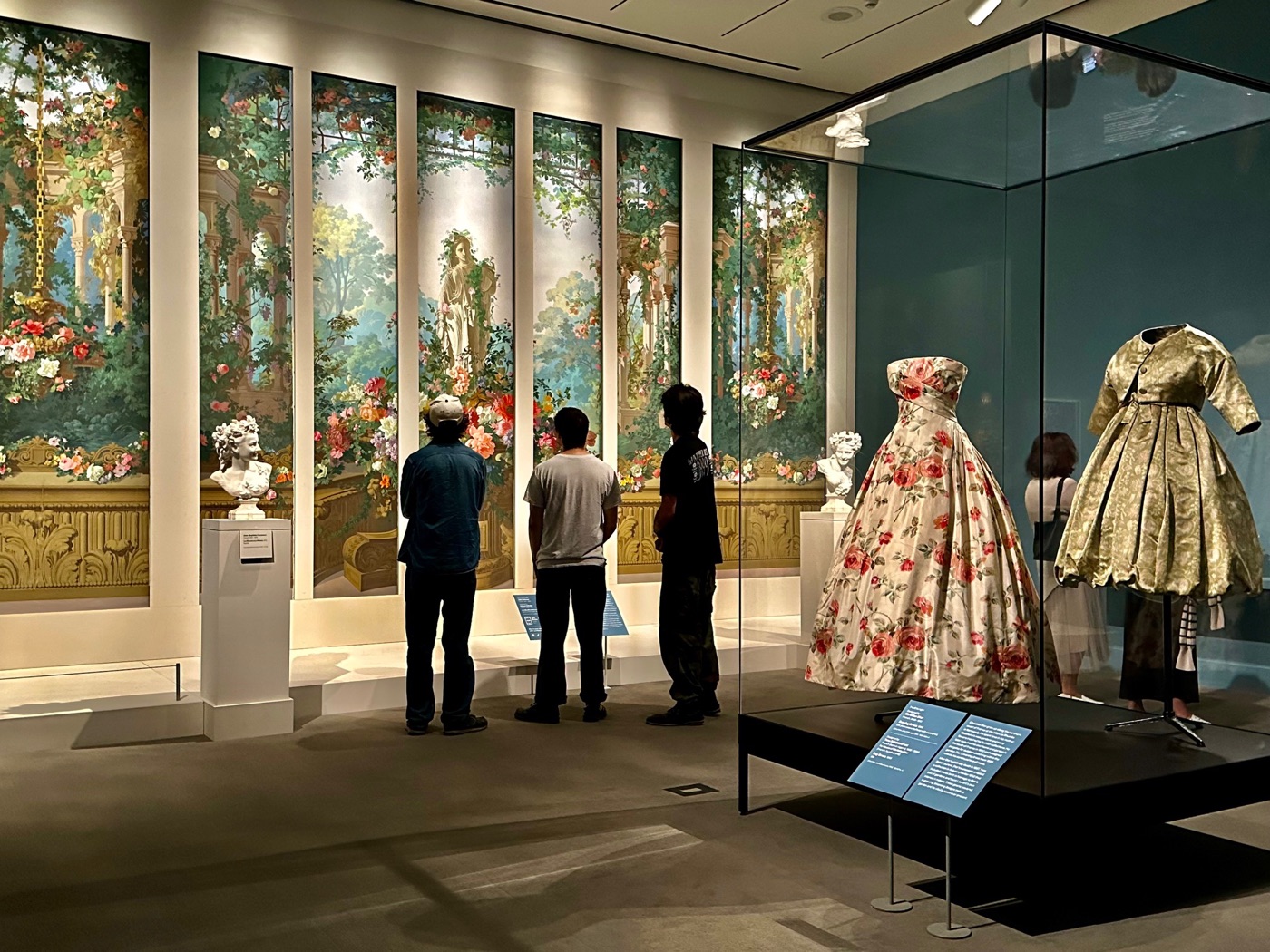 Painted floral panels behind a vitrine of period gowns at Art in Bloom, Museum of Fine Arts, Boston.