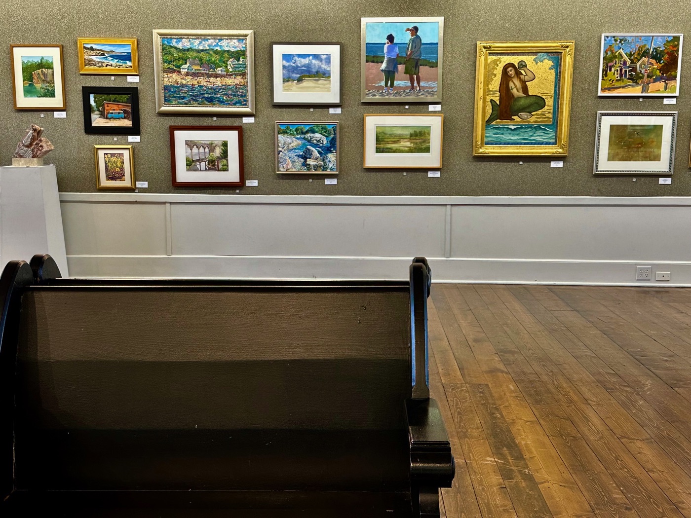 A wall of framed members' paintings above the benches at the North Shore Arts Association, Gloucester.