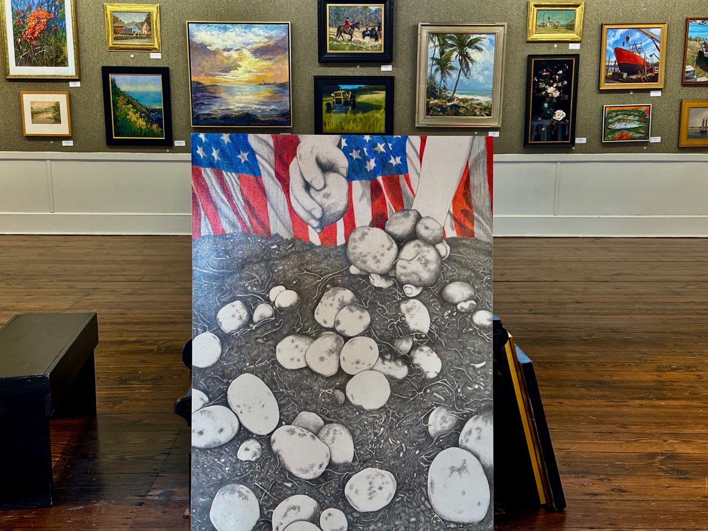 A large mixed-media canvas of hands and an American flag above a field of stones at the North Shore Arts Association.