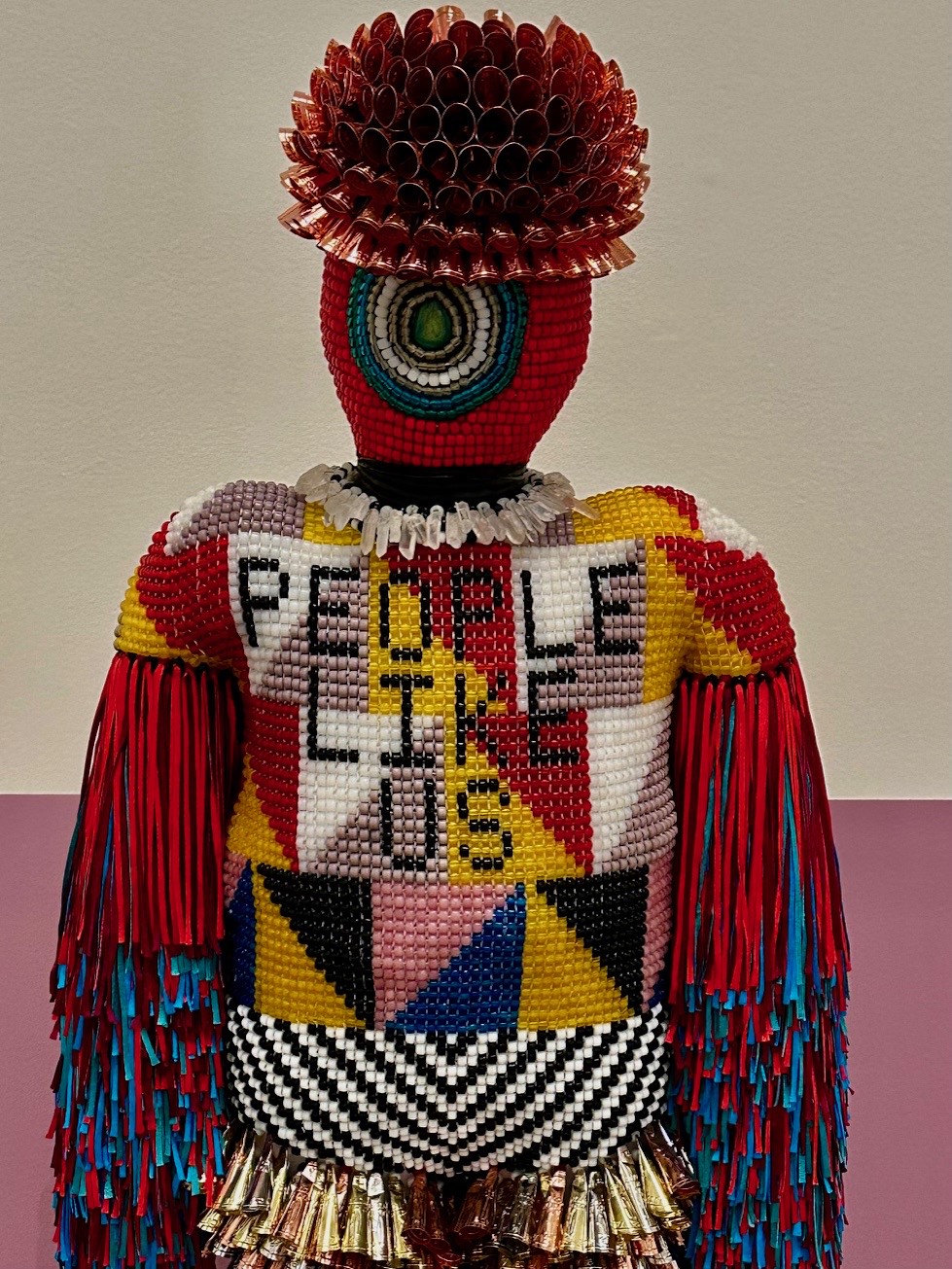 A beaded figure spelling out People Like Us across its chest, from Precious, the Value of Ornament at the Portland Museum of Art.