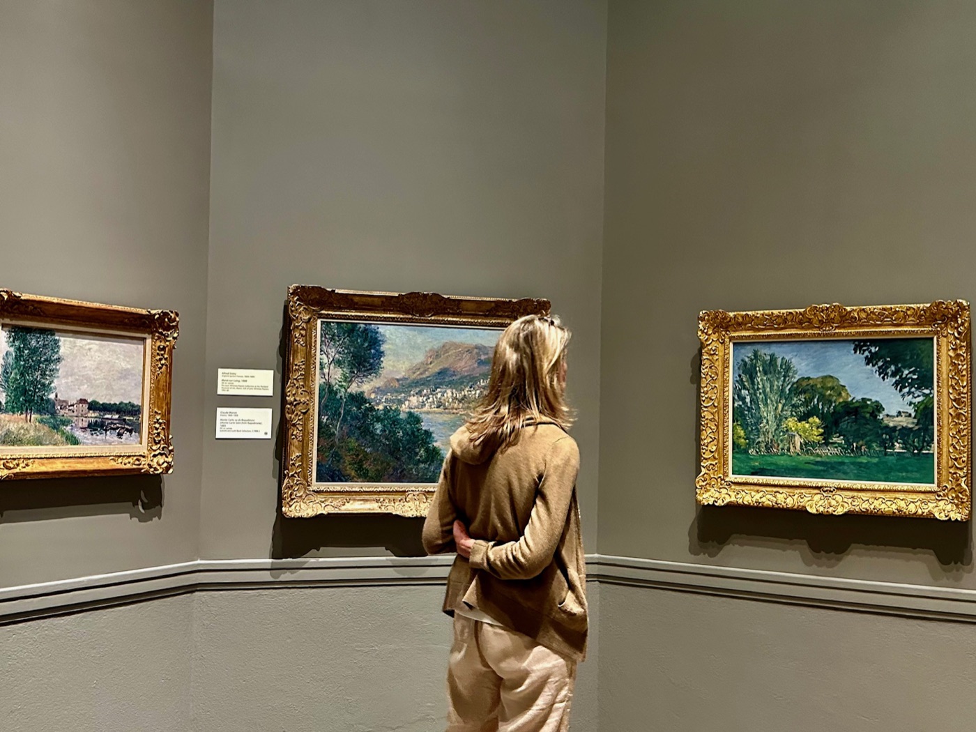 A visitor between gilt-framed Impressionist landscapes by Sisley and Monet at the Portland Museum of Art.