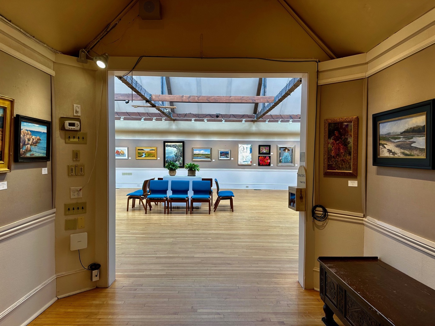 The skylit main gallery of the Rockport Art Association seen through a doorway, paintings hung salon-style, in Rockport.
