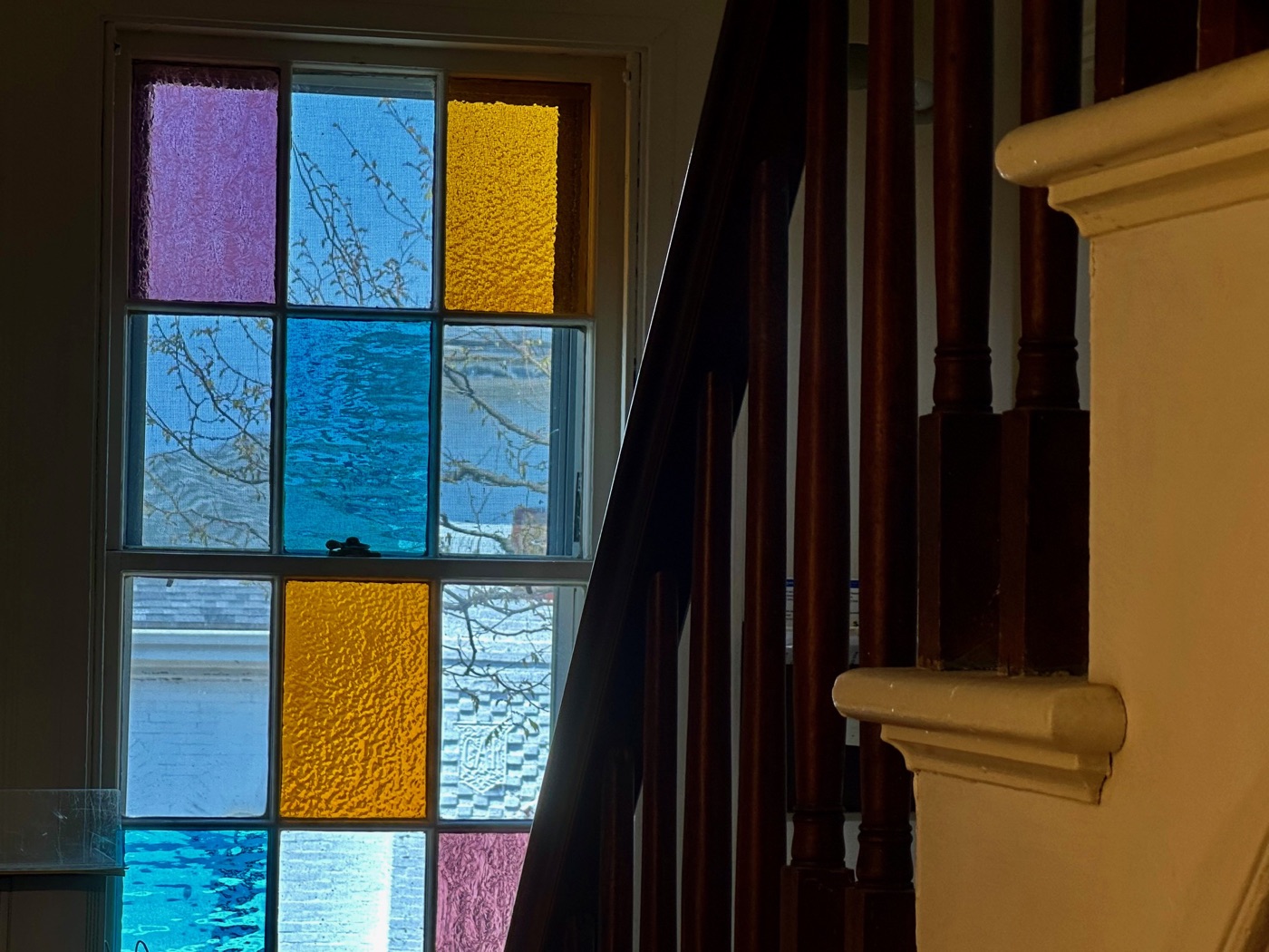 A stained-glass window framed by the staircase banister at the Rockport Art Association.