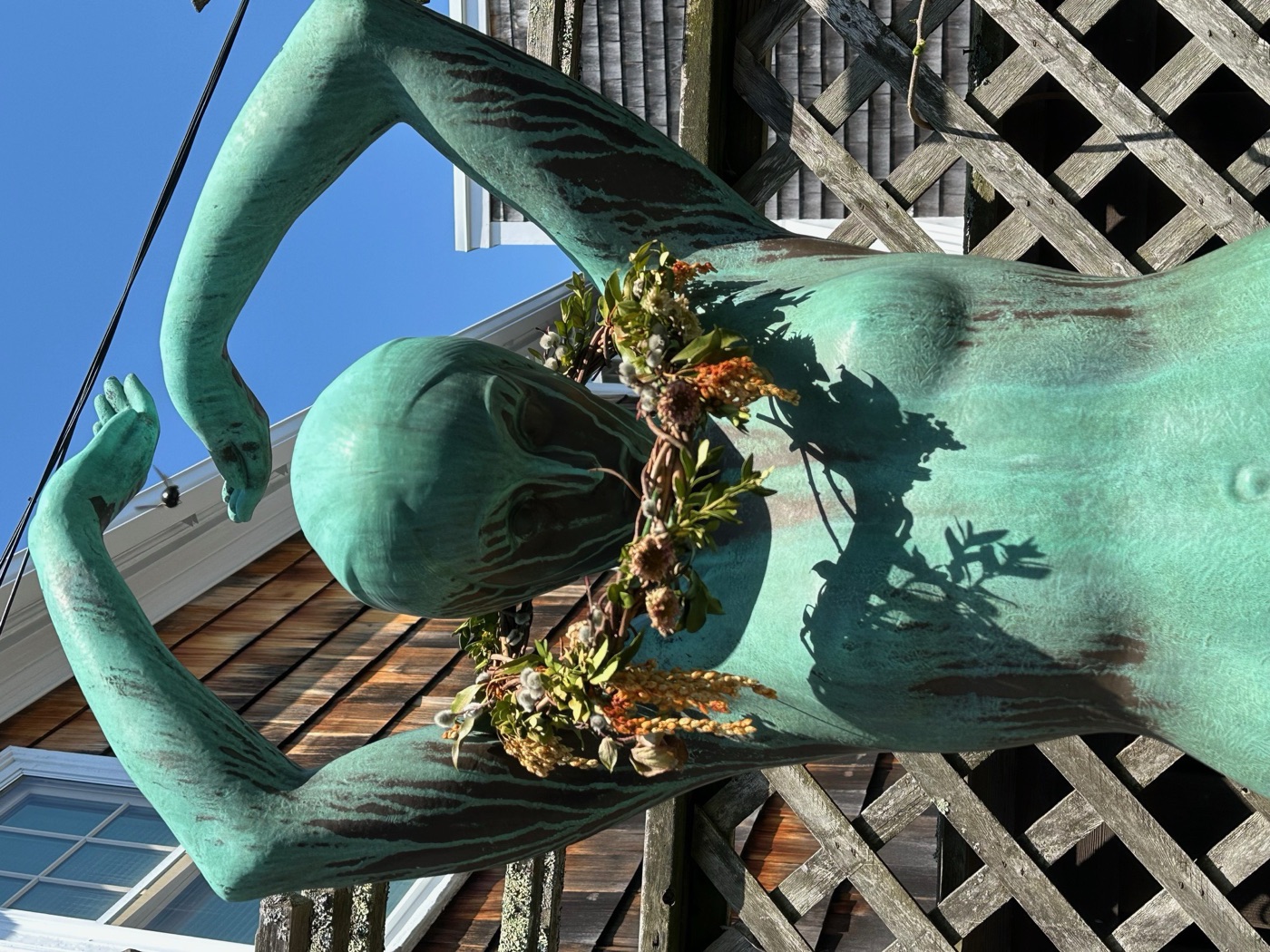 A patinated bronze figure with arms raised, wearing a garland of flowers, at the Rockport Art Association.