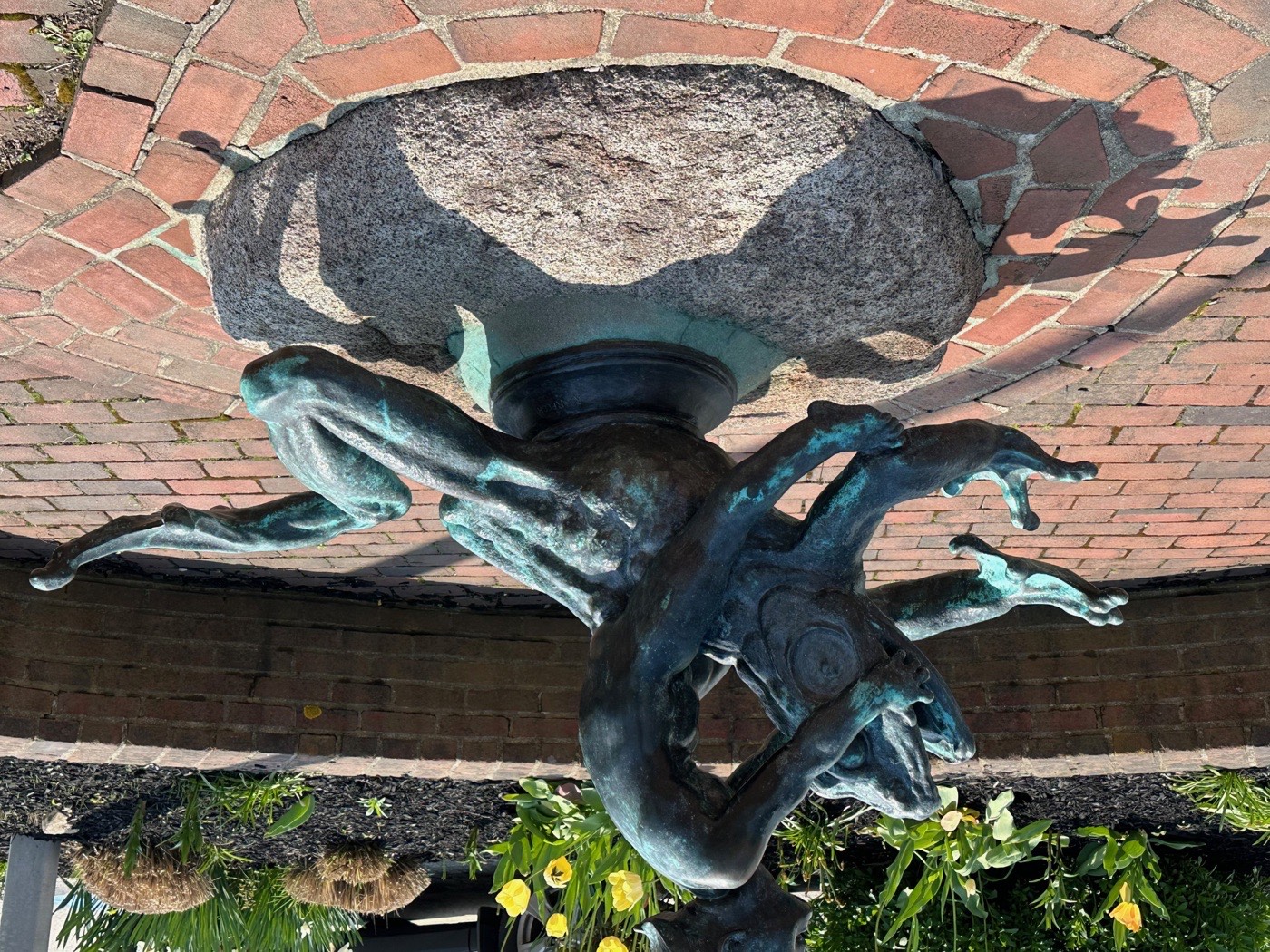 A bronze fountain group beneath a granite basin with daffodils below, at the Rockport Art Association, Rockport.